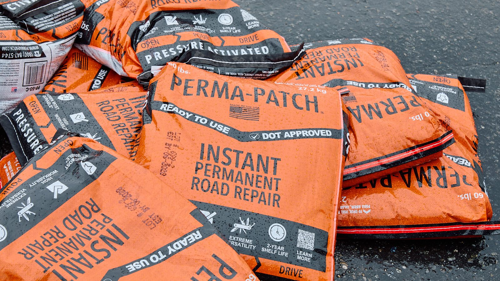 Sixty pound bags of Perma-Patch Regular Mix laid out on wet asphalt, marked ready to use and DOT approved