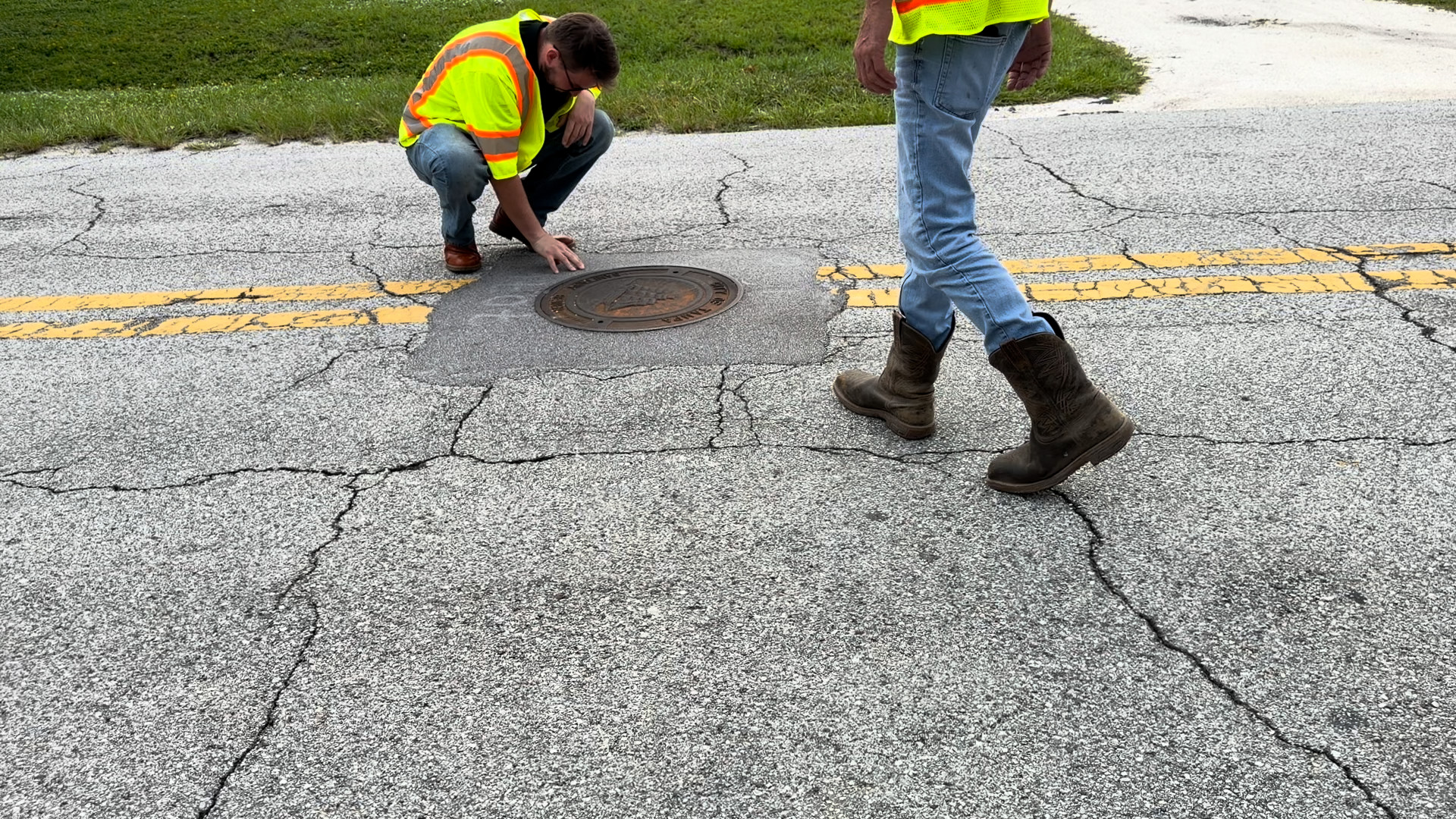 Crew inspecting a 2016 manhole collar at the centerline of a Tampa street, cracking through the surrounding pavement