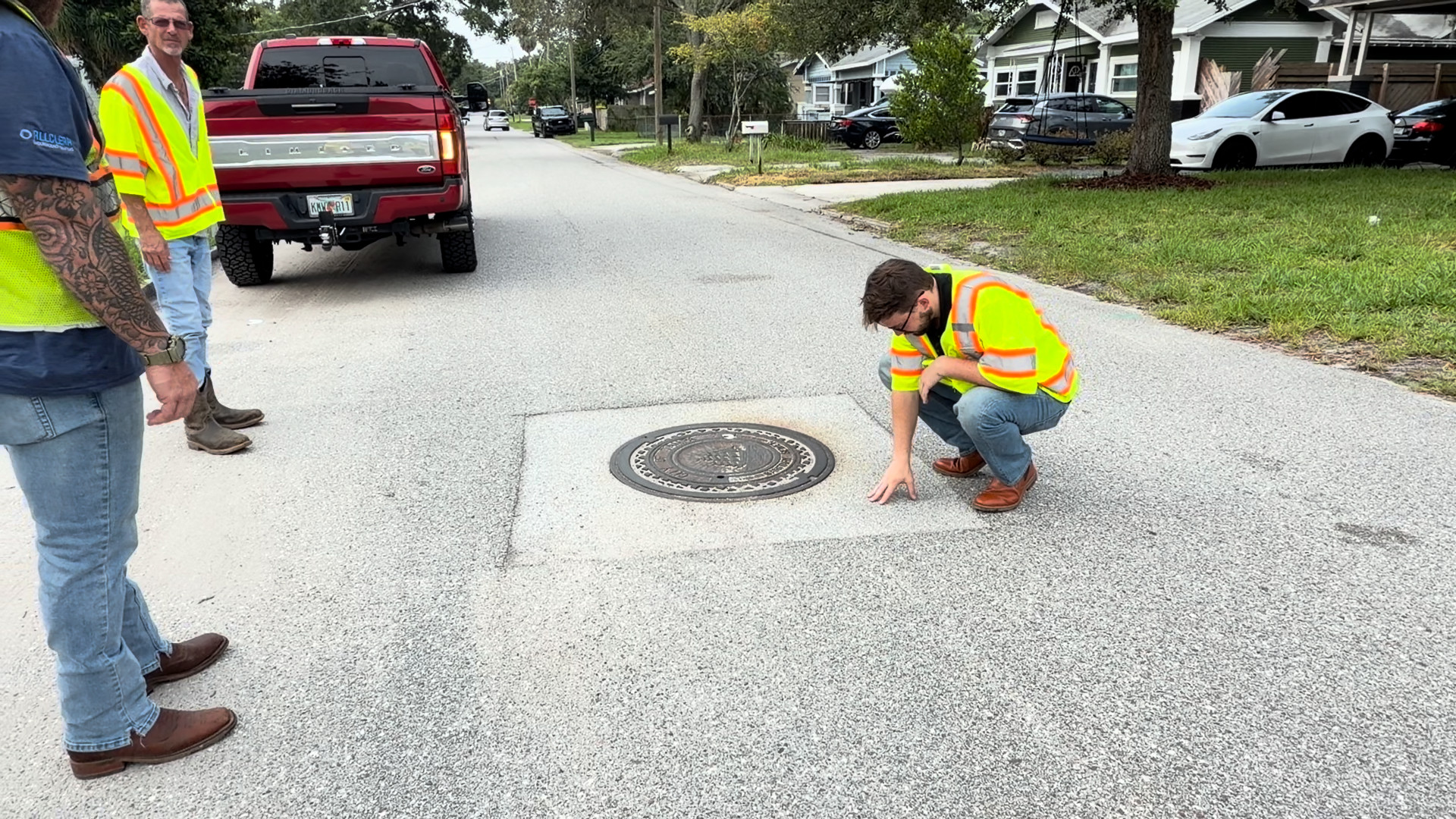 Rowland crew inspecting a manhole repair on a residential Tampa street with the Rowland truck parked behind