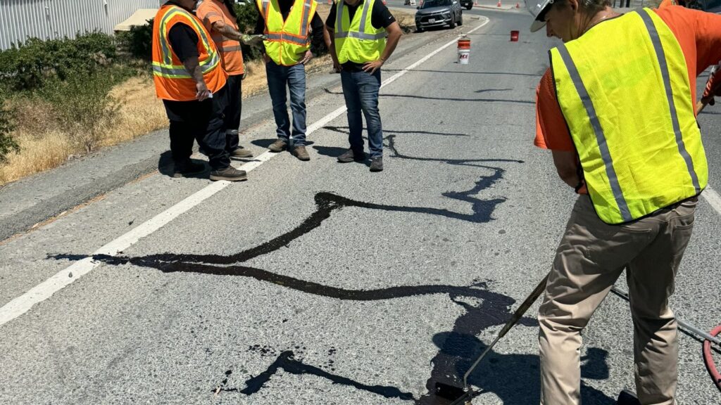 Road crew squeegeeing 6690 ColdFuze cold-pour crack sealant flat over a sealed crack network